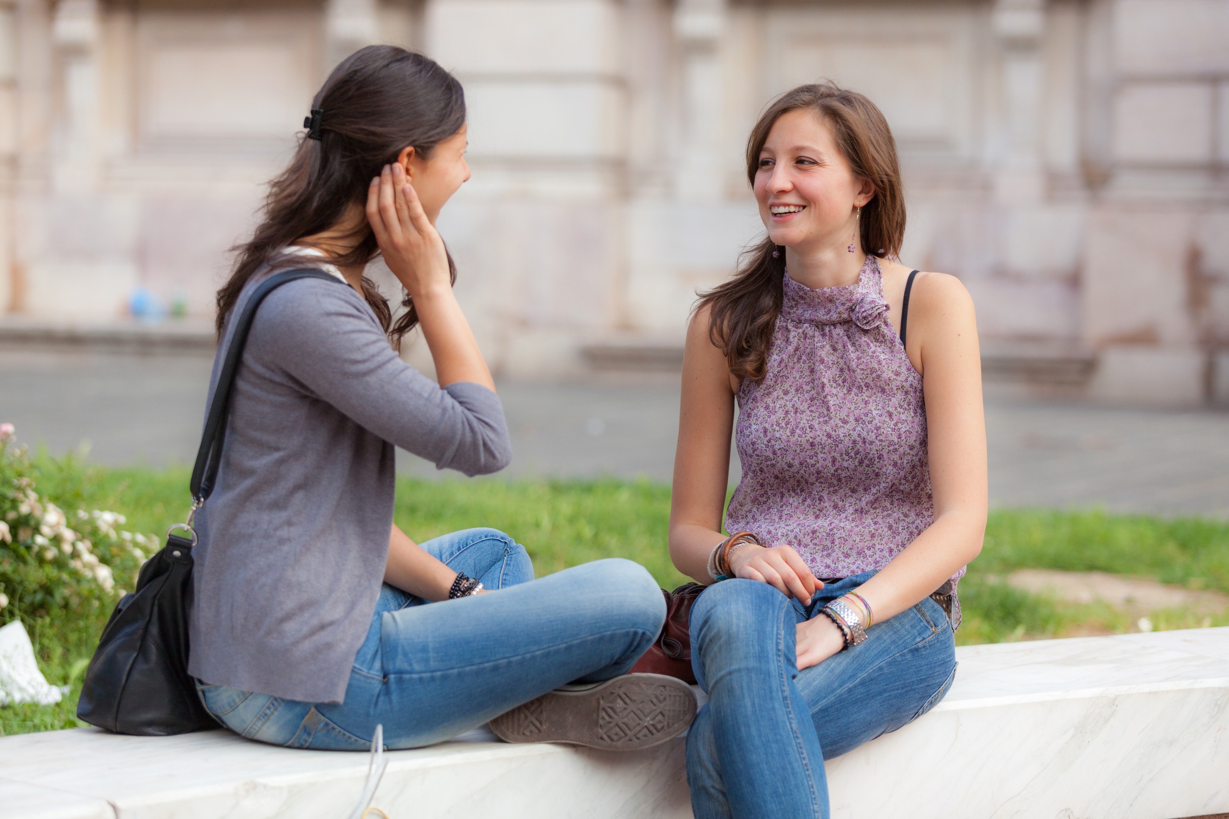 Two young women sitting and talking on a bench in the city.